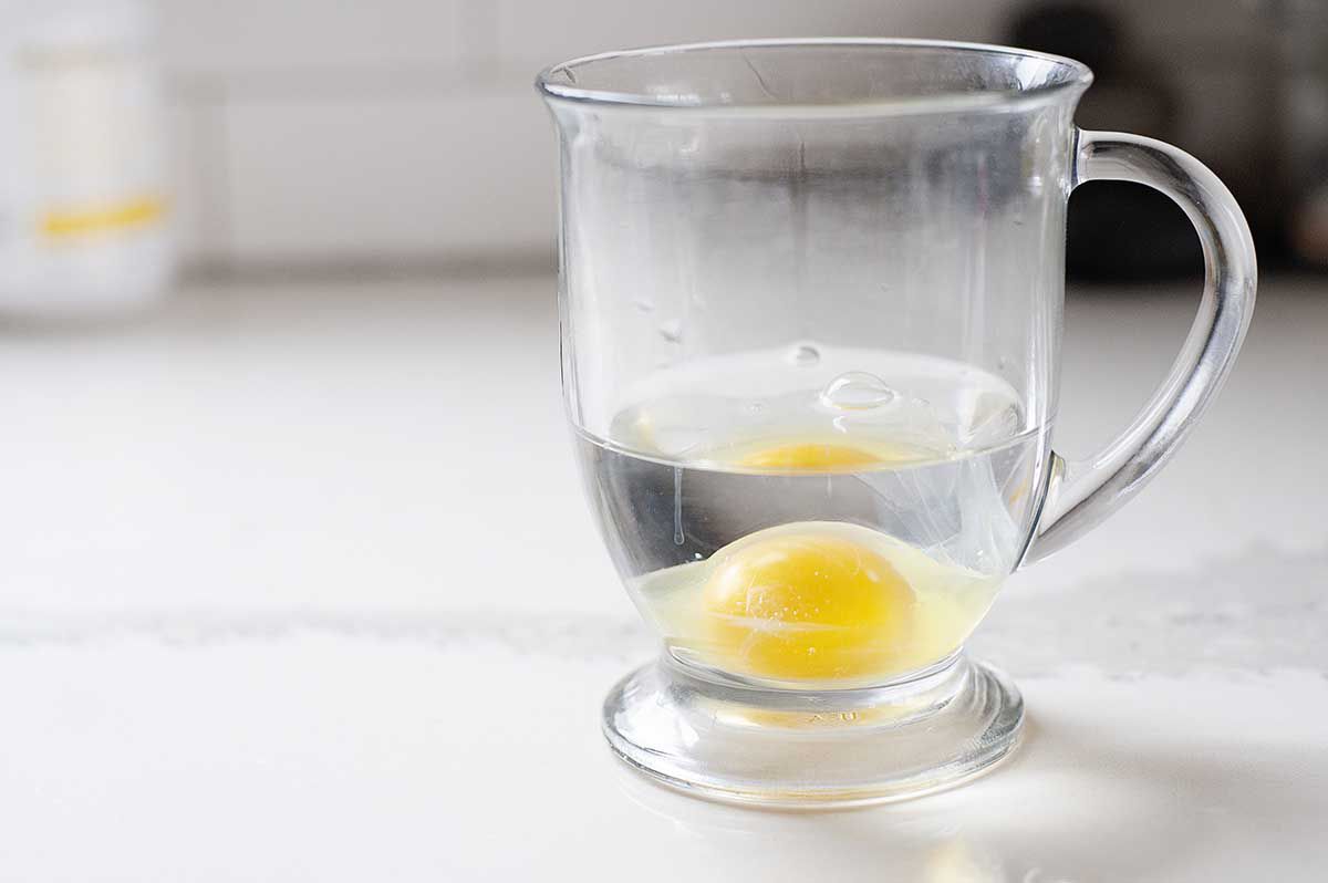 Glass mug with a raw egg and water inside to make a simple poached egg.