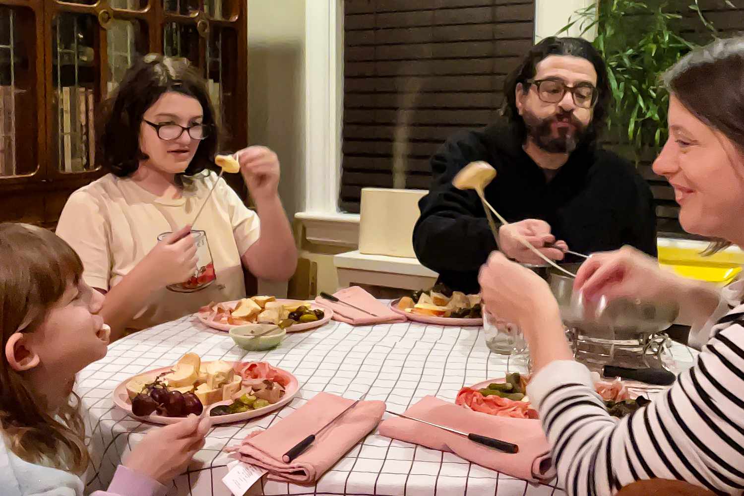 Family around a round dining table enjoying cheese fondue on Valentine's Day
