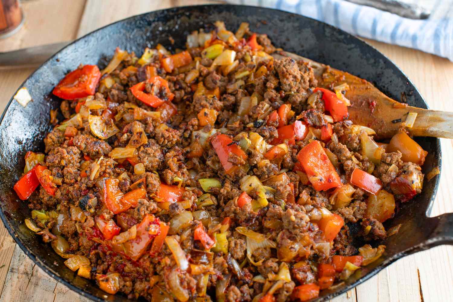 Cooked ground beef with vegetables in a skillet stirred with a wooden spoon