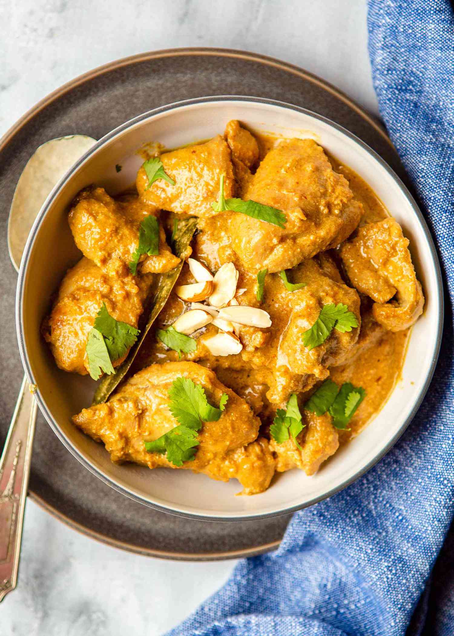 Easy Chicken Korma Recipe - - bowl of chicken with sauce, herbs and almonds