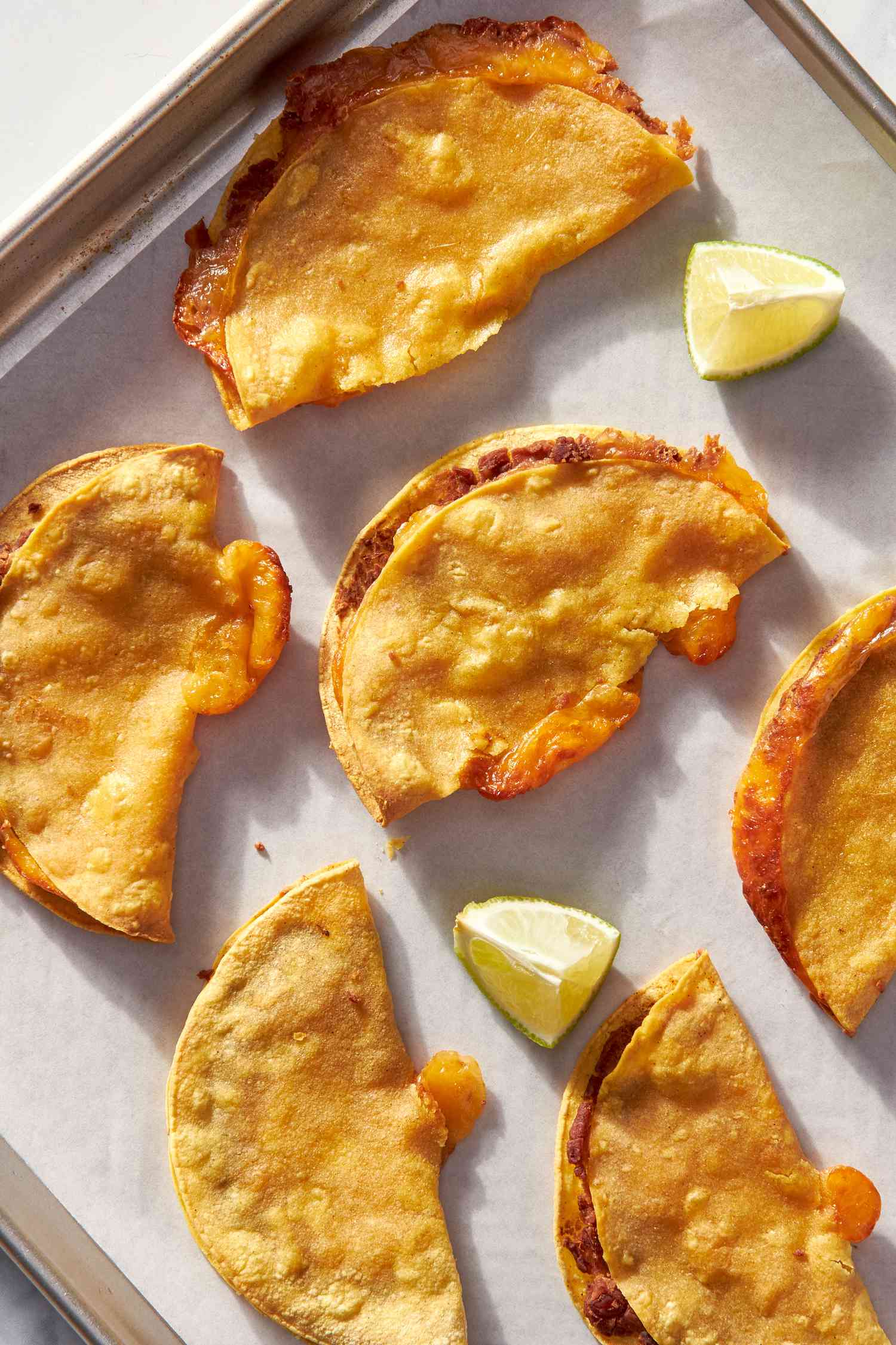Cheesy baked tacos on a parchment paper lined baking sheet with lime wedges
