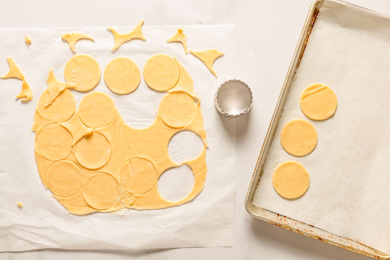 Overhead view of the rolled dough on parchment paper after starting to cut out the cookies with a cookie cutter and place on a baking sheet for Sand Tarts recipe
