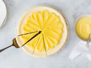 Lemon Cheesecake - whole cheesecake with lemon curd on top and someone is about to take a slice out of it