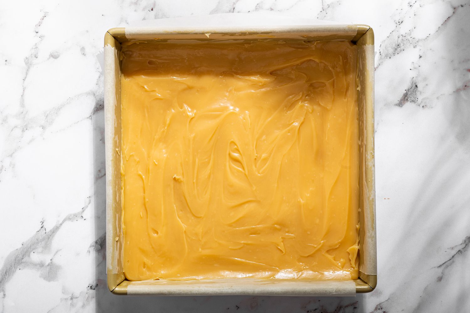 Overhead view of a baking pan showing the caramel mixture spread onto the baked shortbread for Millionaire Shortbread recipe