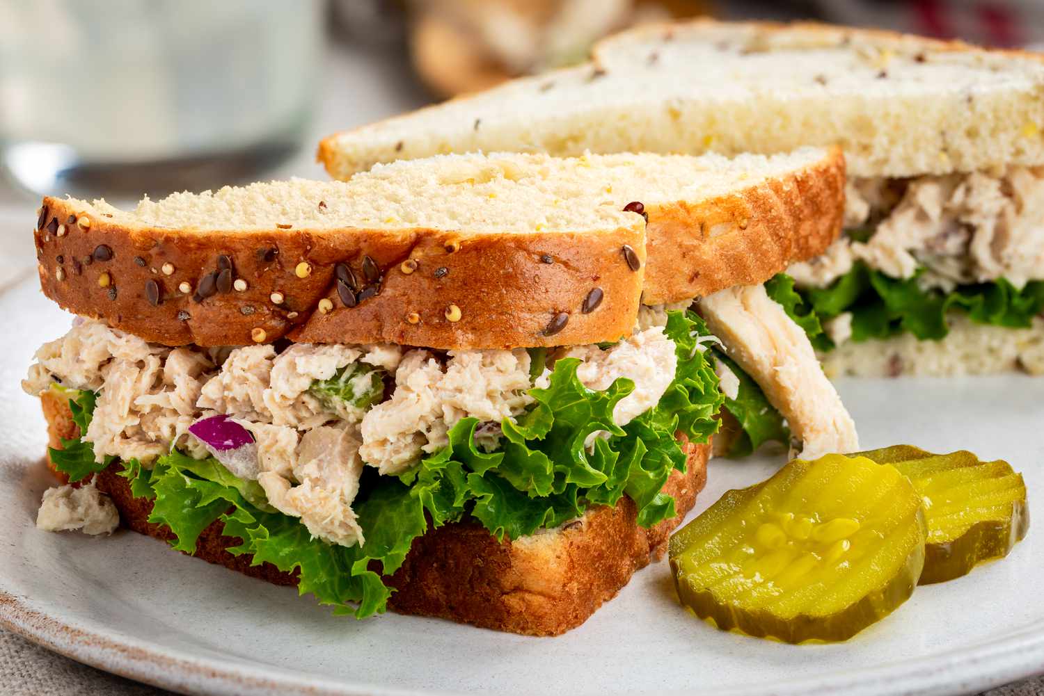 Side view of a tuna salad sandwich with sliced pickles on a white plate