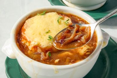 A bowl of French onion soup topped with melted cheese and herbs served with a spoon