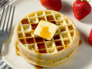 round waffles stacked on a plate with butter, syrup, and fruit