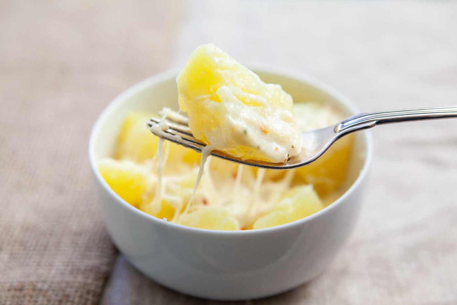 A fork pulling a cheesy bite from a ramekin of Pepper Jack Potatoes