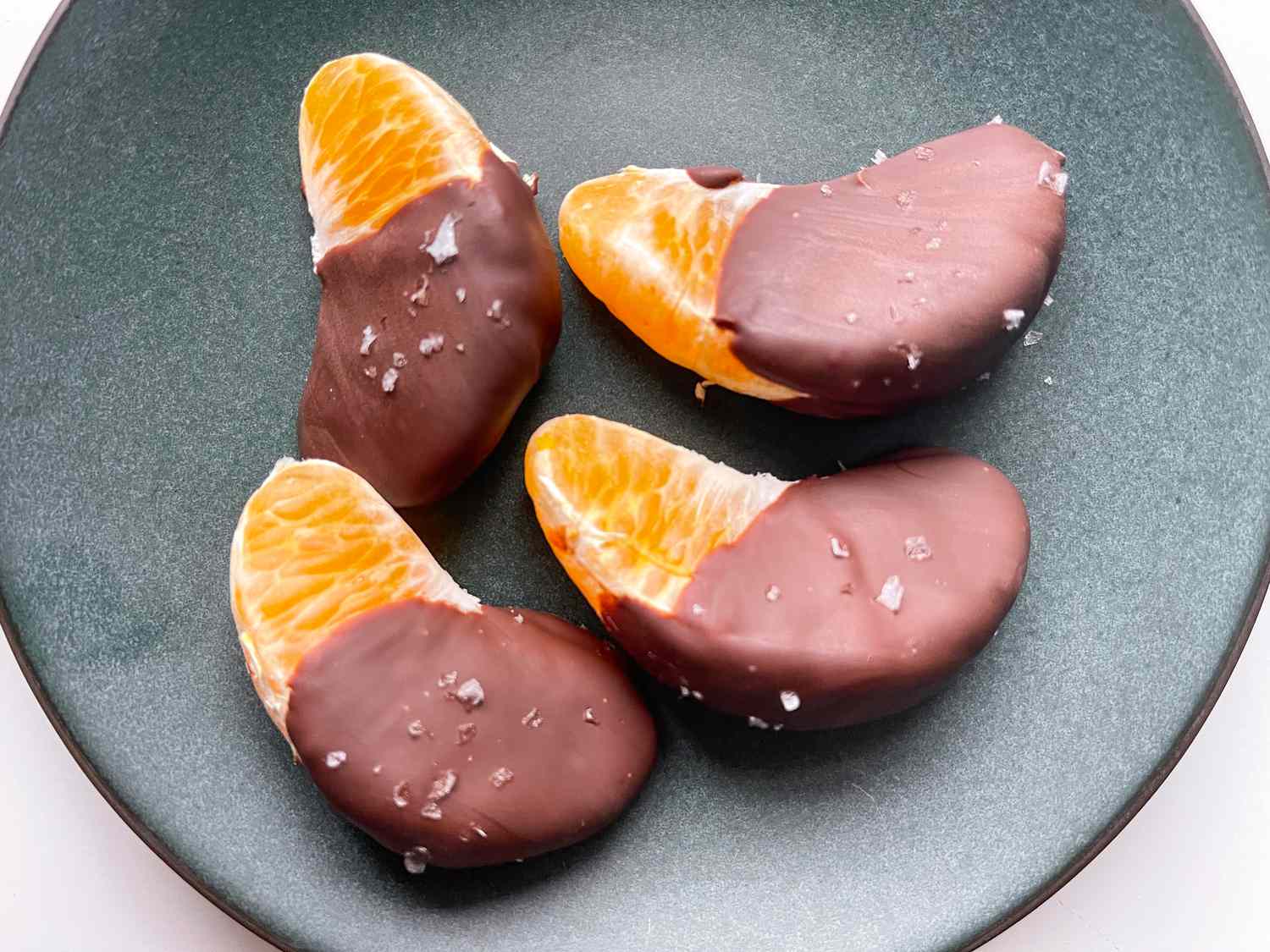 Overhead view of a small gray plate of four orange slices that have been dipped in chocolate and sprinkled with salt