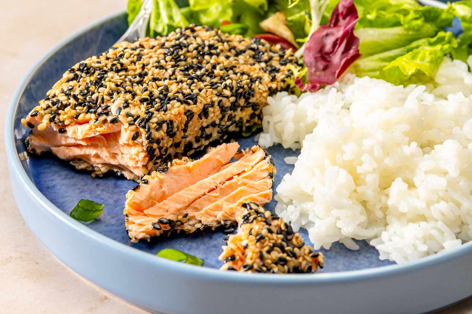 Sesame-crusted salmon served with rice and a salad on a blue plate