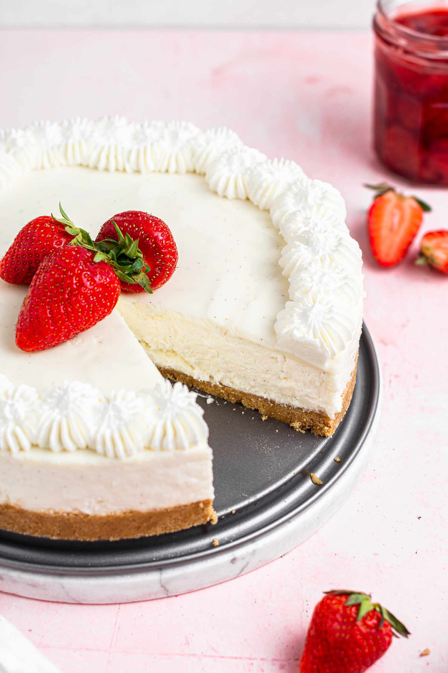 An easy no bake cheesecake with a slice removed and set on a pink background.