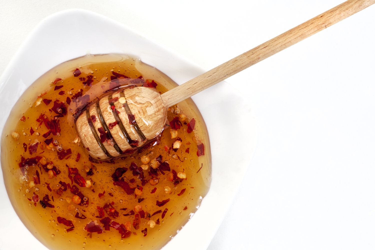 A dish of honey infused with chili flakes wooden honey dipper resting inside