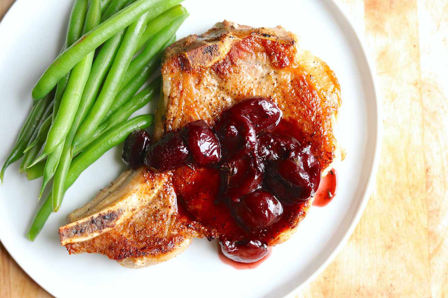 A plate with green beans and a pork chop with cherry sauce, ready to serve and eat