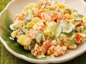 A bowl of potato salad with cucumbers and carrots on a green plate