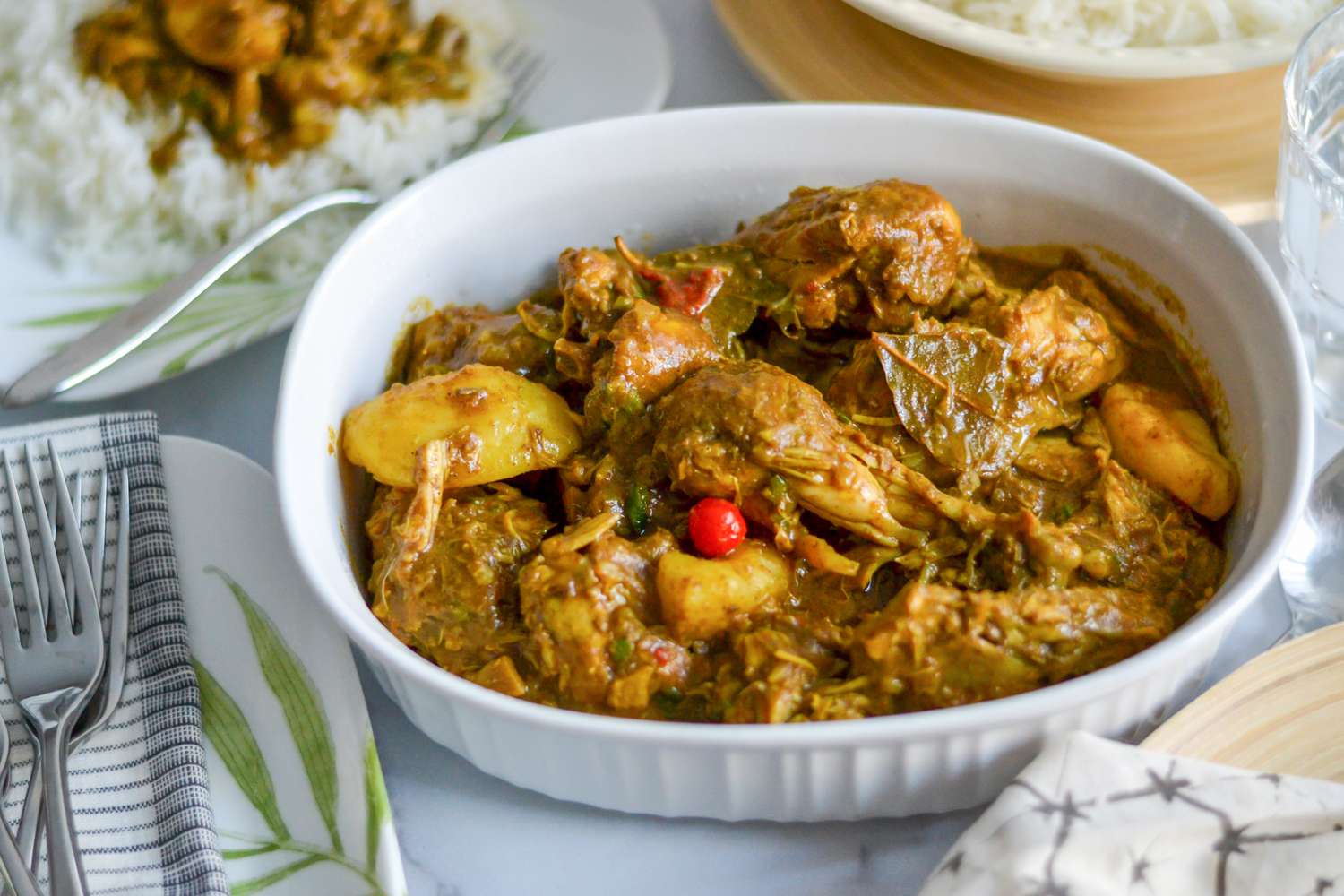 Guyanese Chicken Curry in a Baking Dish Surrounded by a Bowl of Rice and a Plate with a Serving