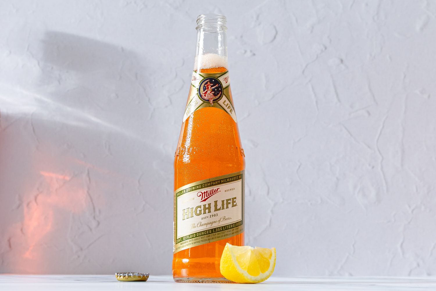 A bottle of Miller High Life beer with a lemon wedge and bottle cap on a table