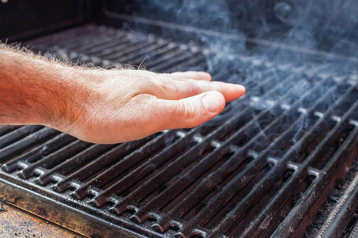 A hand checking the heat of a smoking grill
