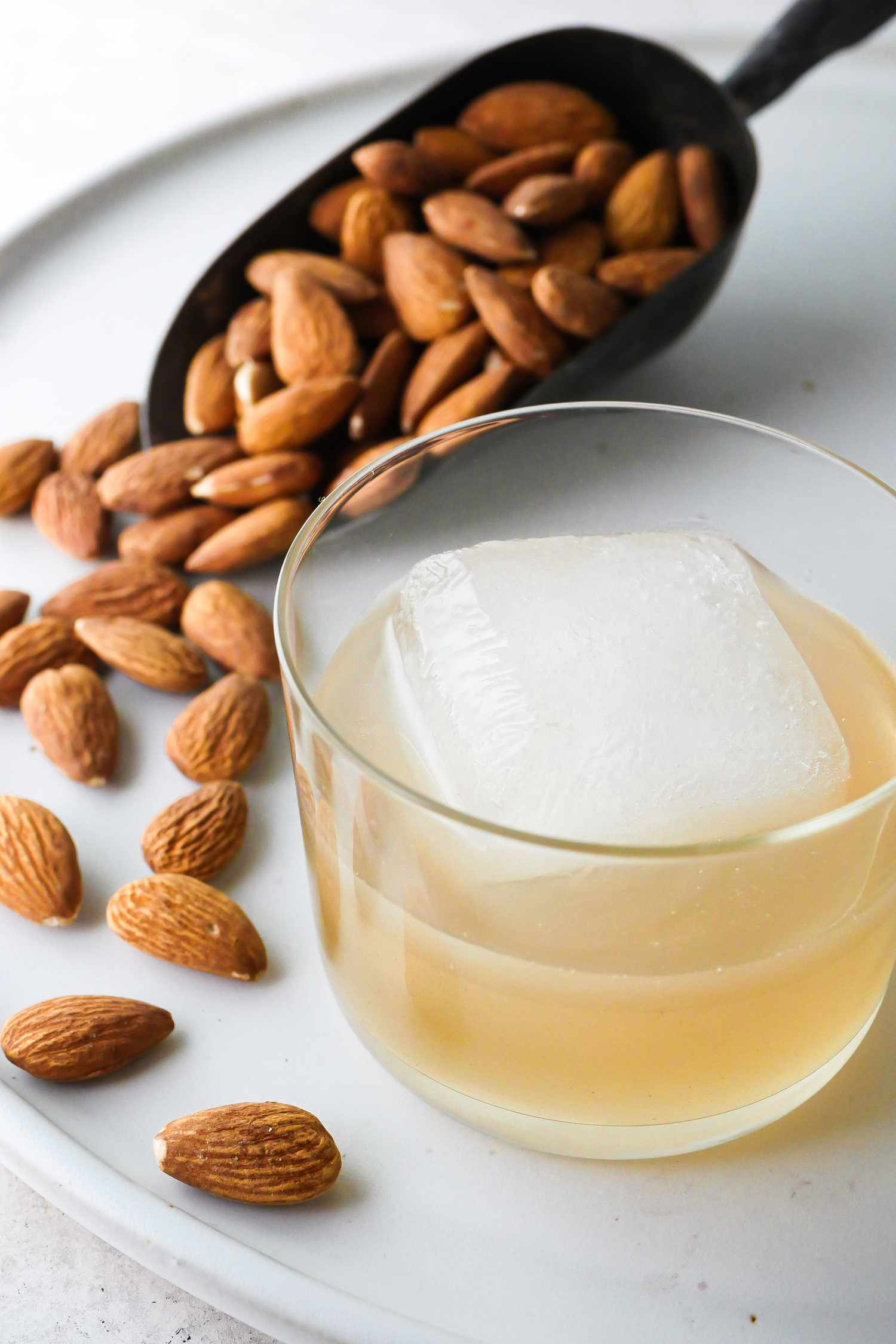 A cocktail using Orgeat almond syrup next to a scoop of raw almonds.