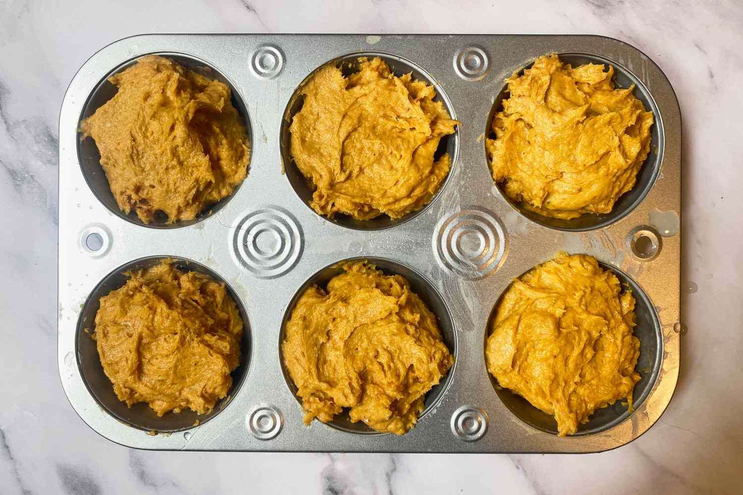 Muffin tin filled with pumpkin batter before baking