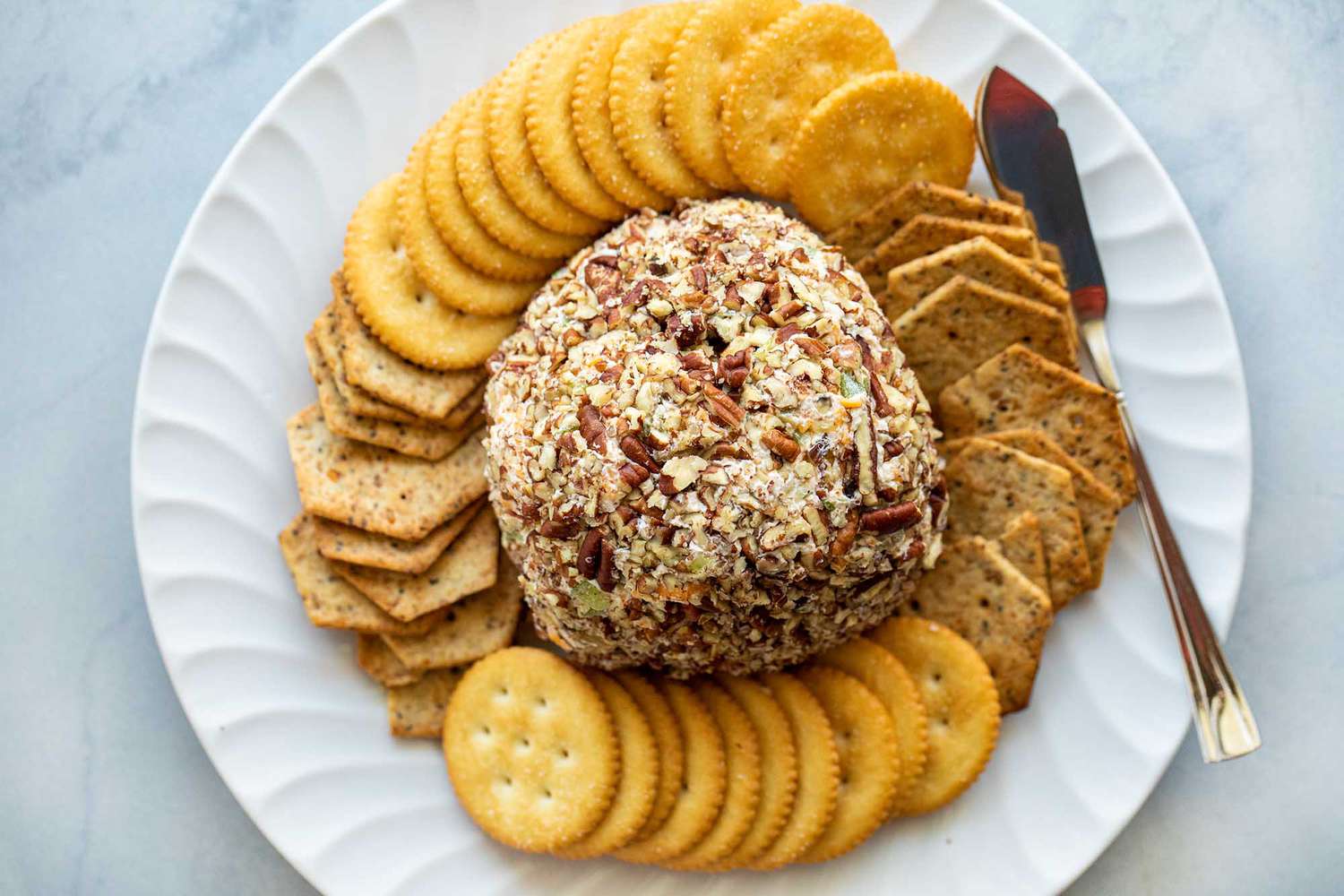 A cheeseball ready to serve with crackers and a cheese knife