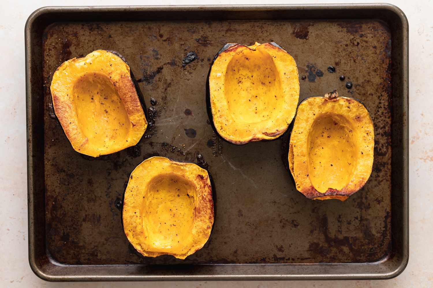 Halved acorn squash roasting on a baking sheet to make vegetarian stuffed squash.