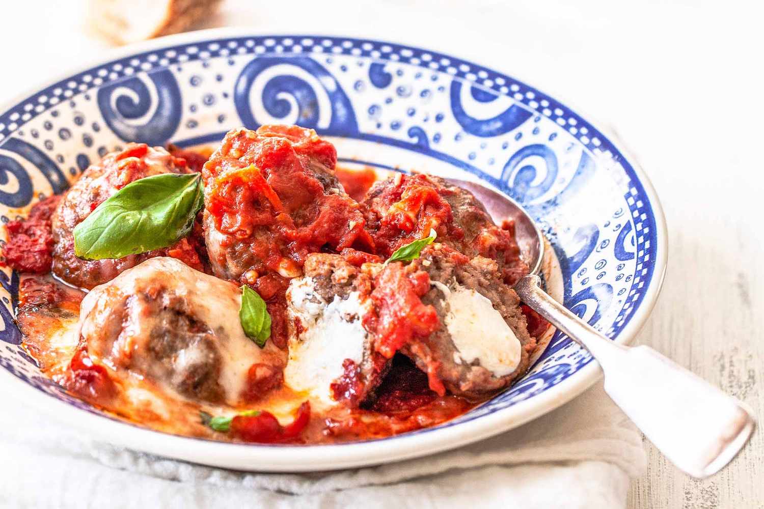 Mozzarella stuffed meatballs in a blue and white bowl with a spoon