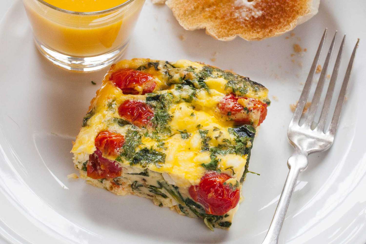 Frittata Square with Spinach, Tomatoes, and Feta on a plate with a fork and orange juice
