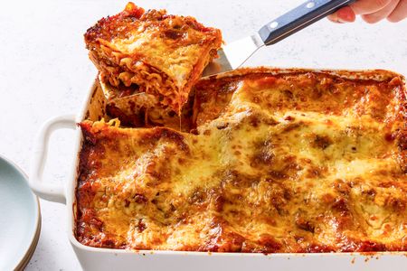 A dish of baked lasagna with a portion being lifted out using a spatula