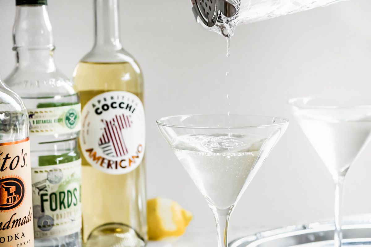 Vesper Cocktail Poured into a Martini Glass from a Mixing Glass and to the Left, Bottles of Vodka, Gin, and Americano
