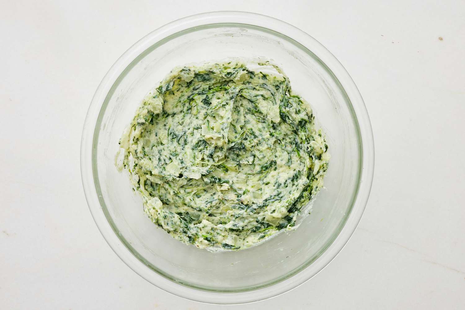 Three-fourths of cooked spinach mixed with cheese and seasoning in a bowl for spinach flornetine breakfast casserole recipe