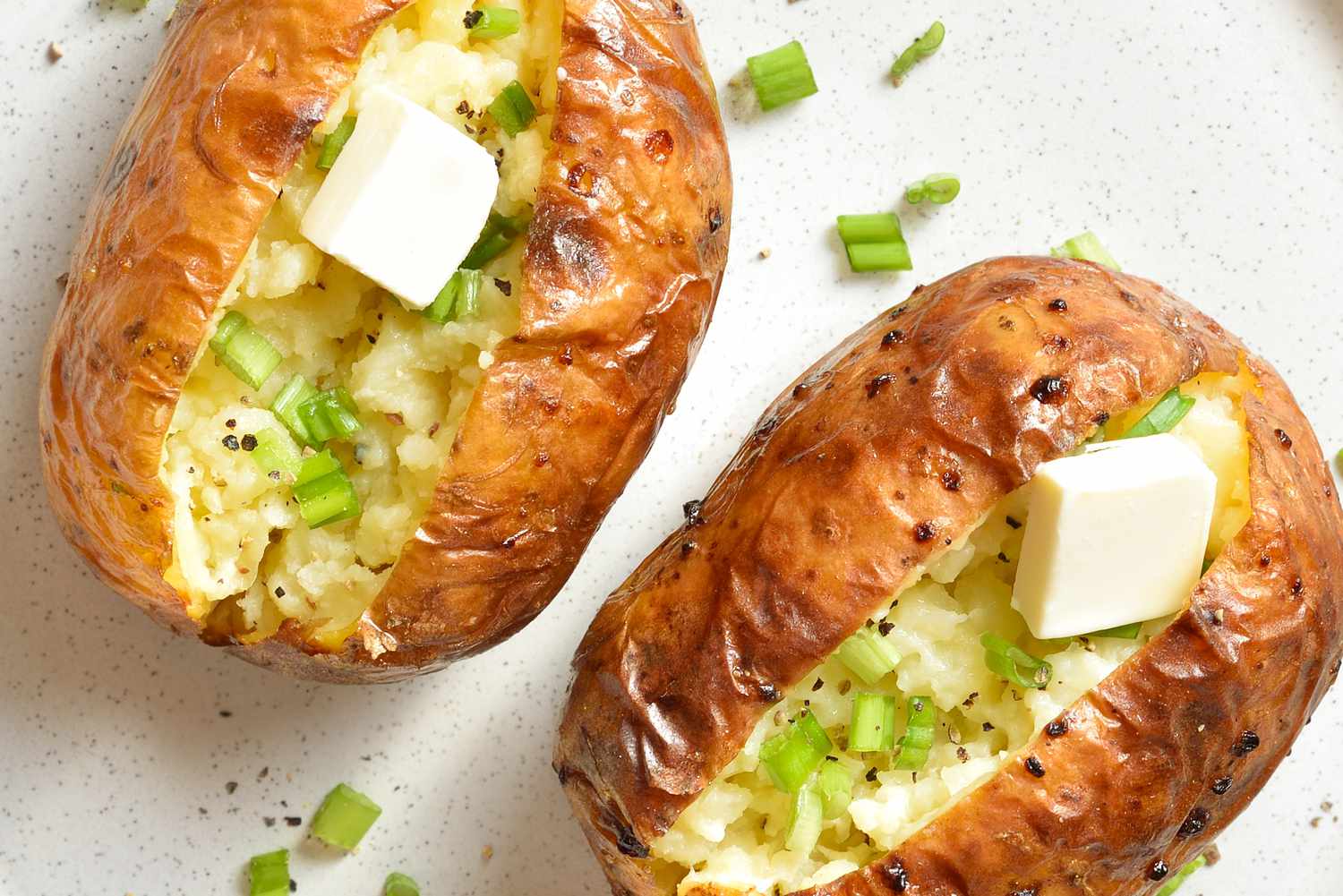 Two baked potatoes stuffed with butter and fresh green onions