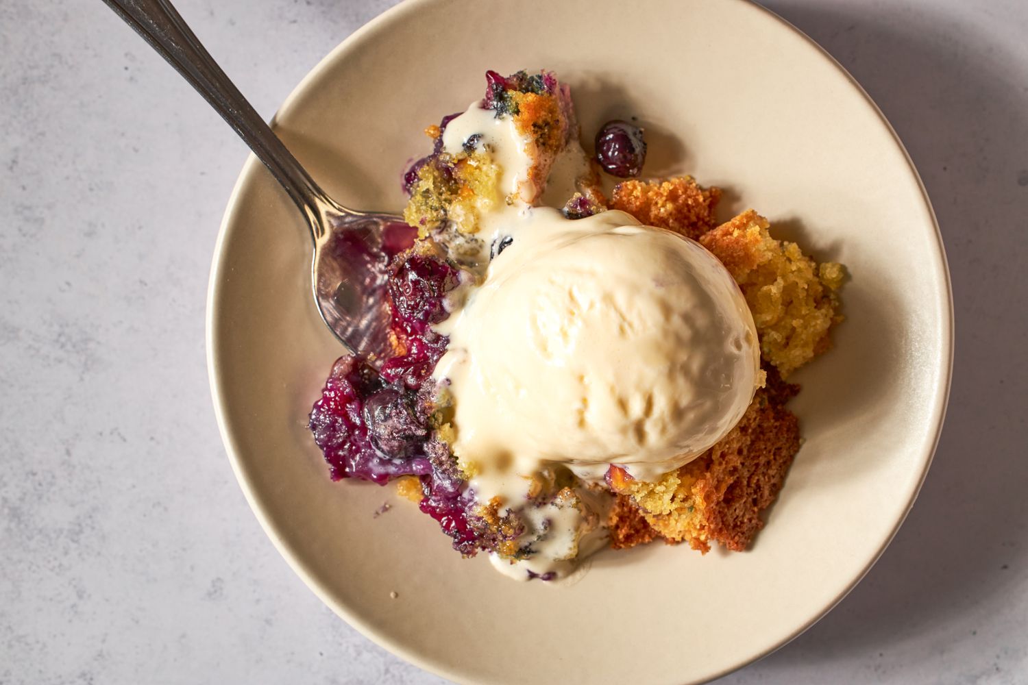 A plate of blueberry corn spoon cake served with a scoop of ice cream and a spoon