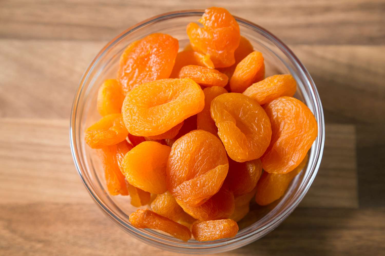 A bowl with dried apricots on a wooden background