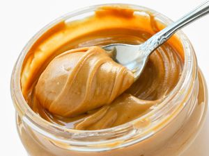 A close up shot of an open jar of peanut butter with a spoon taking out a scoop
