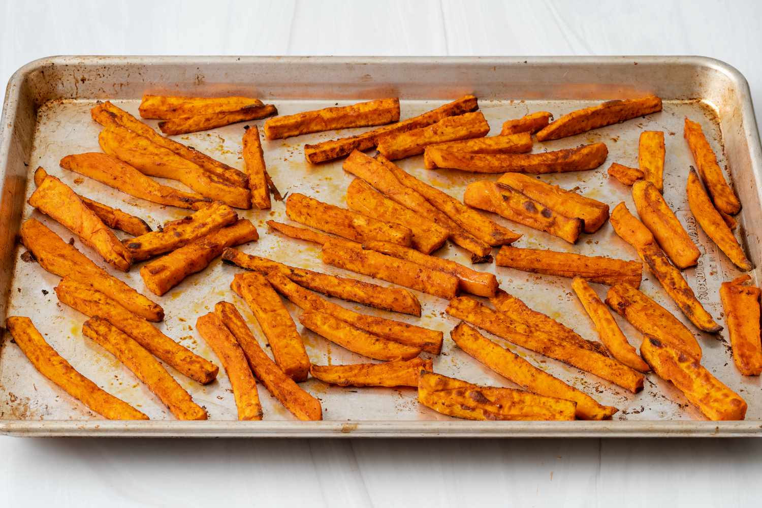 Cooked sweet potato fries resting on a baking sheet.