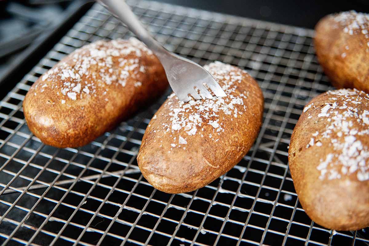 Four salted potatoes on a wire rack with a fork stuck in the center potato 