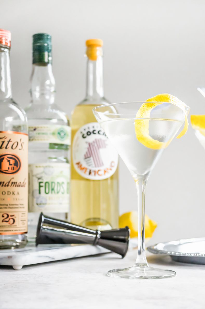 Vesper Cocktail with a Lemon Peel Surrounded by Vesper Cocktail Ingredients (Vodka, Americano, and Gin) 