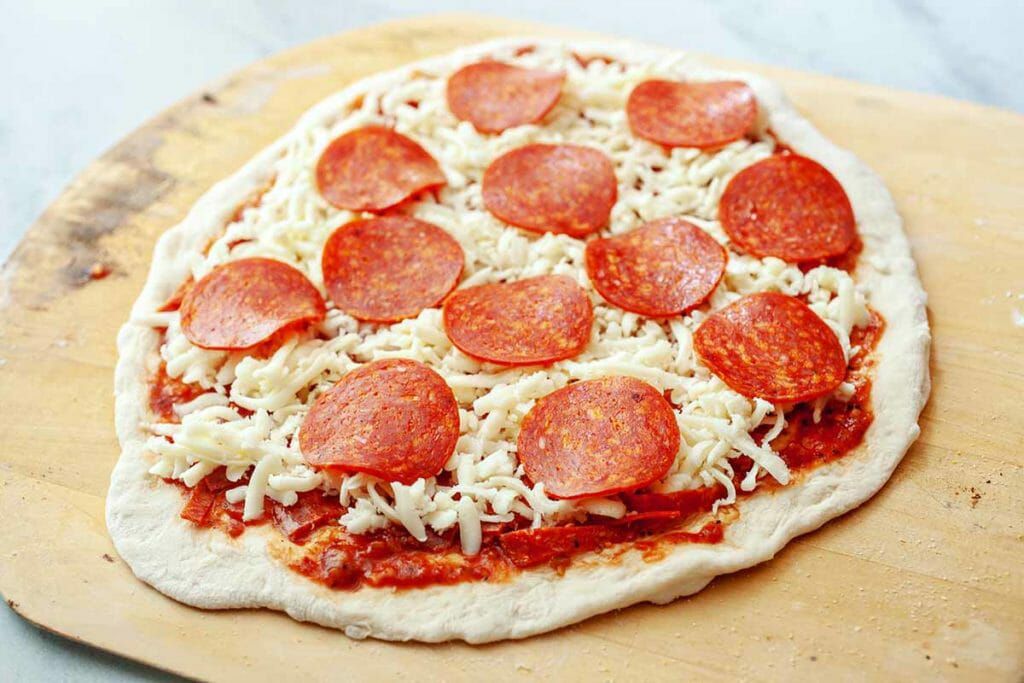 Assembling homemade pepperoni pizza