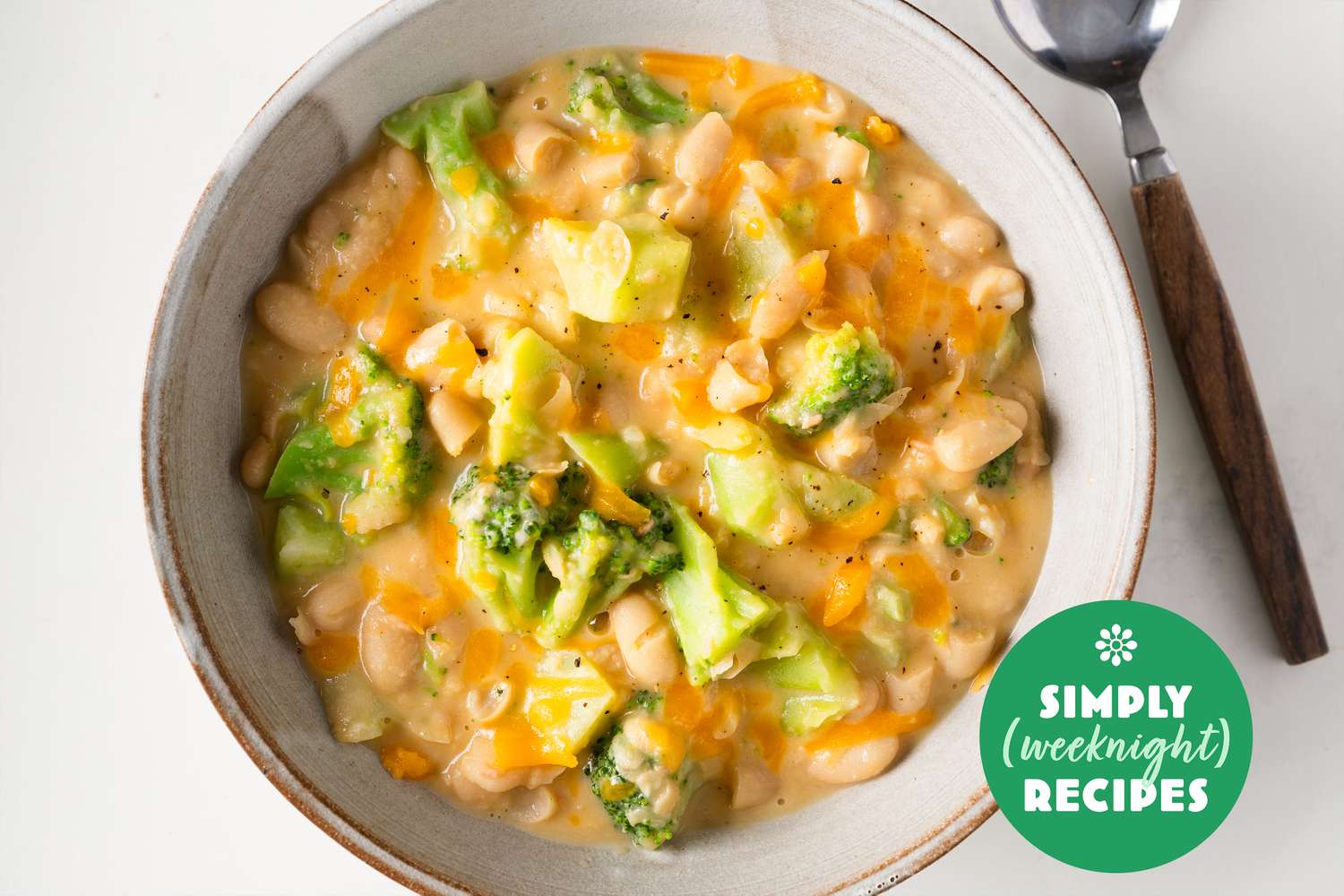 Broccoli and cheese white beans in a pale serving bowl with a spoon on the side