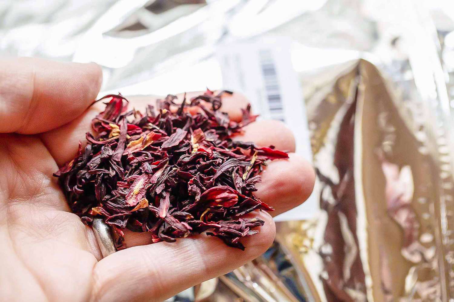 Dried hibiscus is displayed on the palm of a hand. The hand is held above the plastic containers it came in.