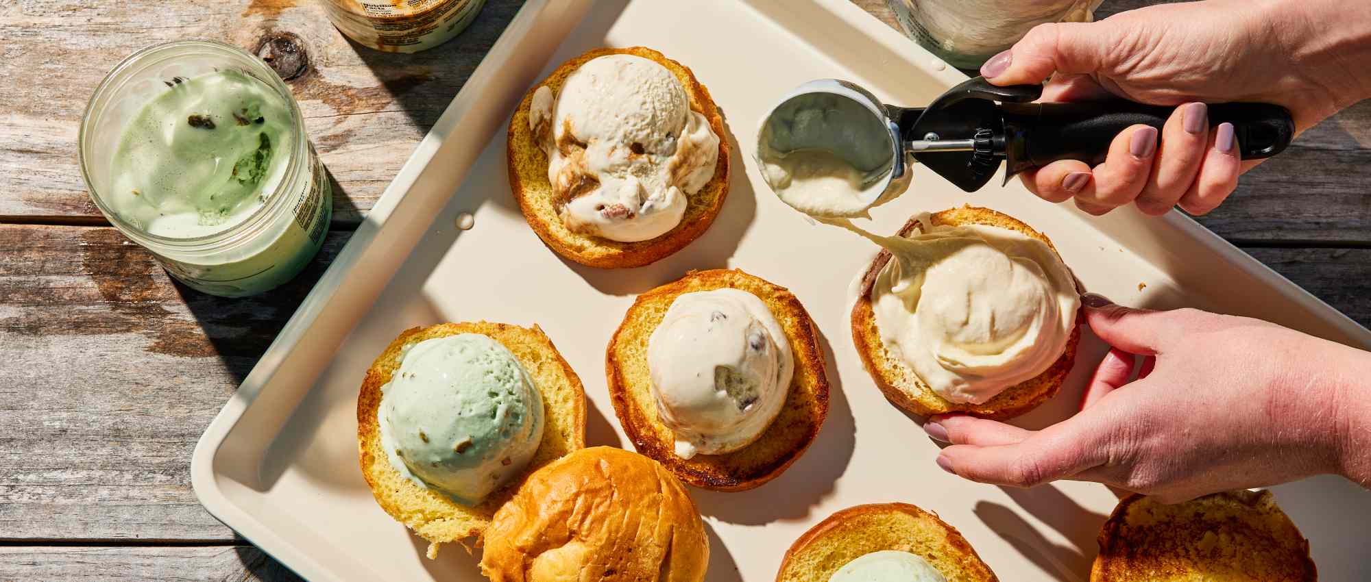 Tray of ice cream scoops placed on buns, with a hand scooping ice cream