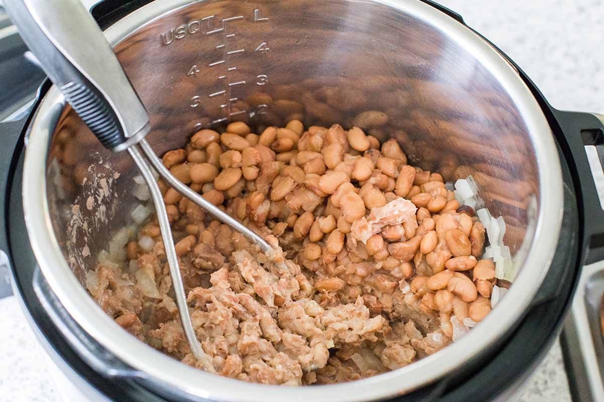 Mashing cooked beans in the bottom of the instant pot.