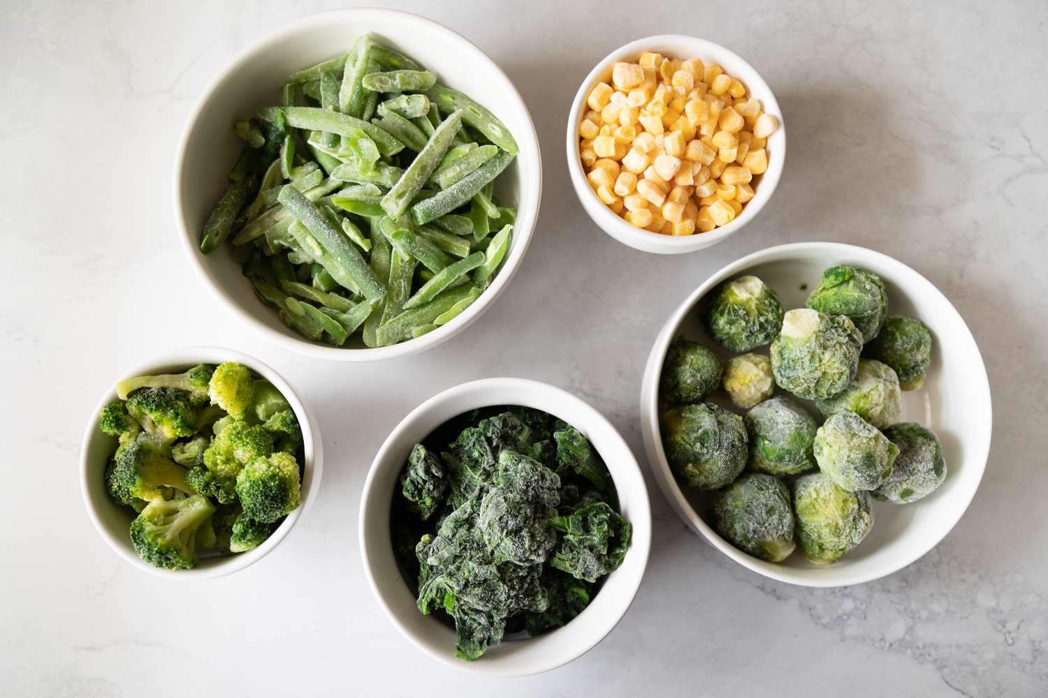 Frozen corn green beans broccoli brussels sprouts in white bowls