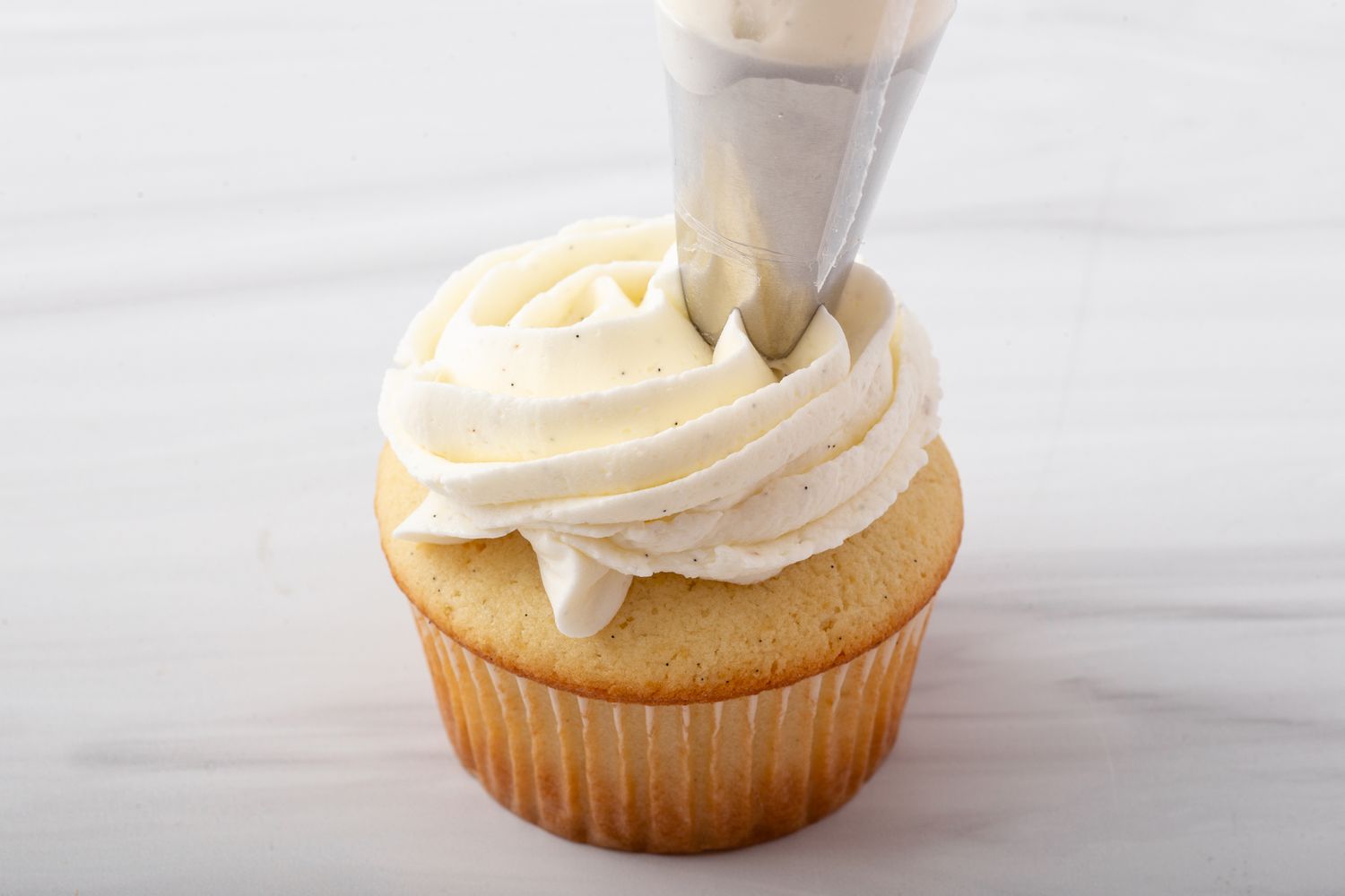 Piping vanilla buttercream on a vanilla cupcake.