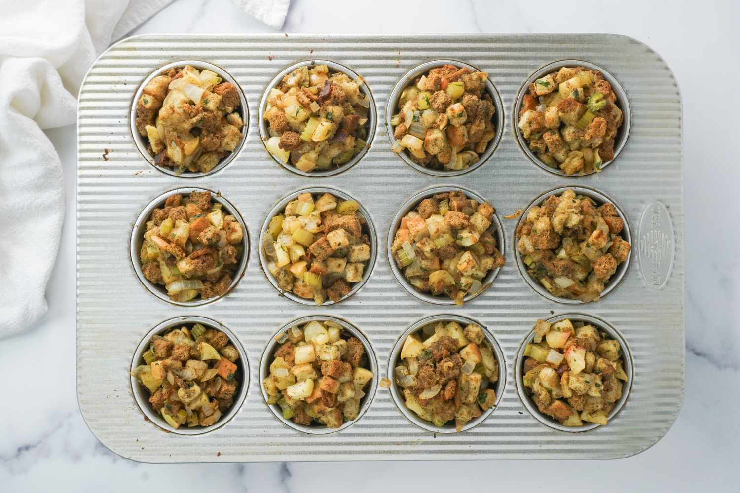 A baking tray with 12 compartments filled with stuffing muffin portions