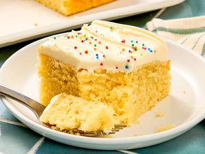 A slice of yellow cake with frosting and sprinkles on a plate with a fork holding a piece of the cake