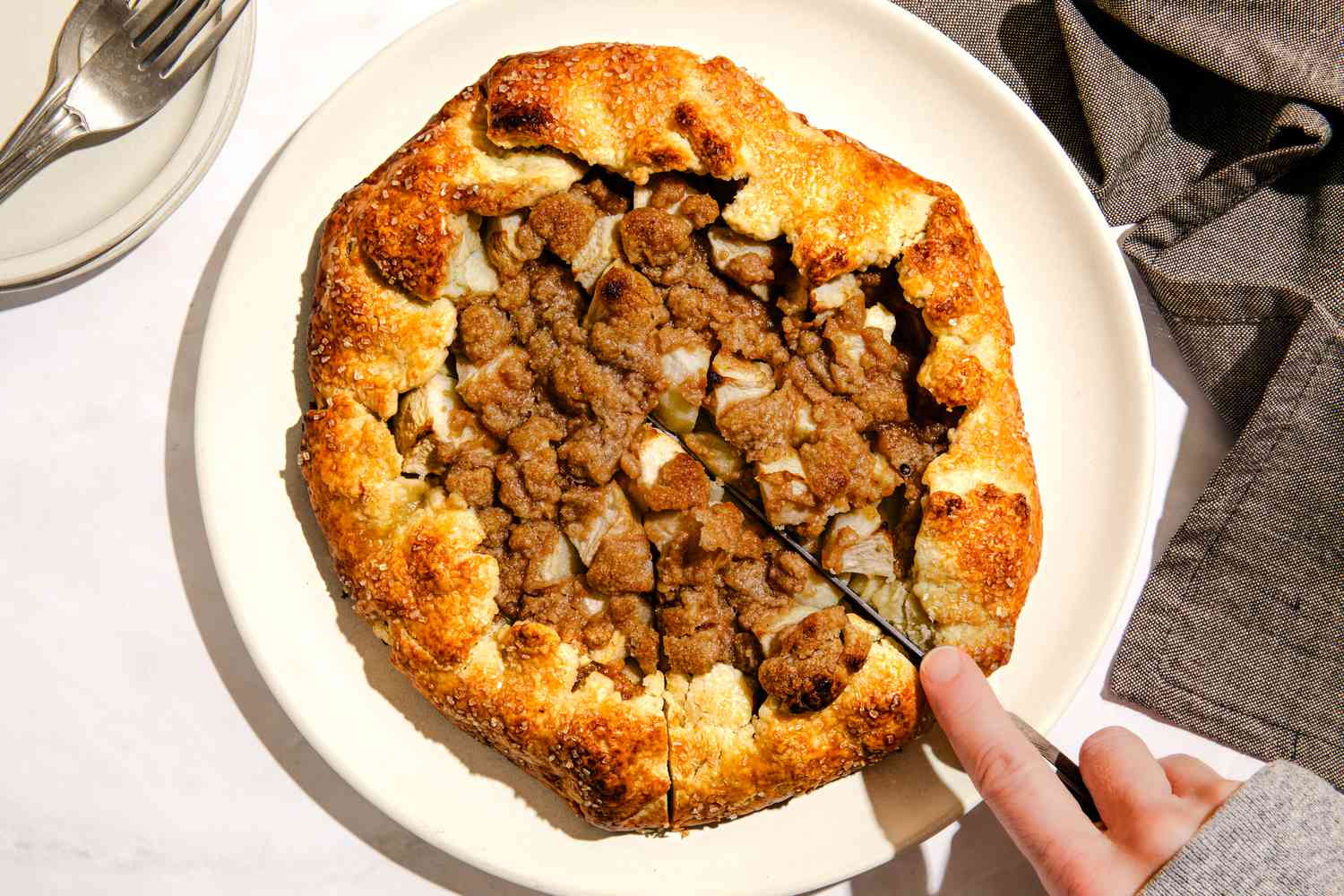 Somone cutting into Ina Garten's apple crostada on a plate (at a table setting with a stack of plates with forks and a table napkin)