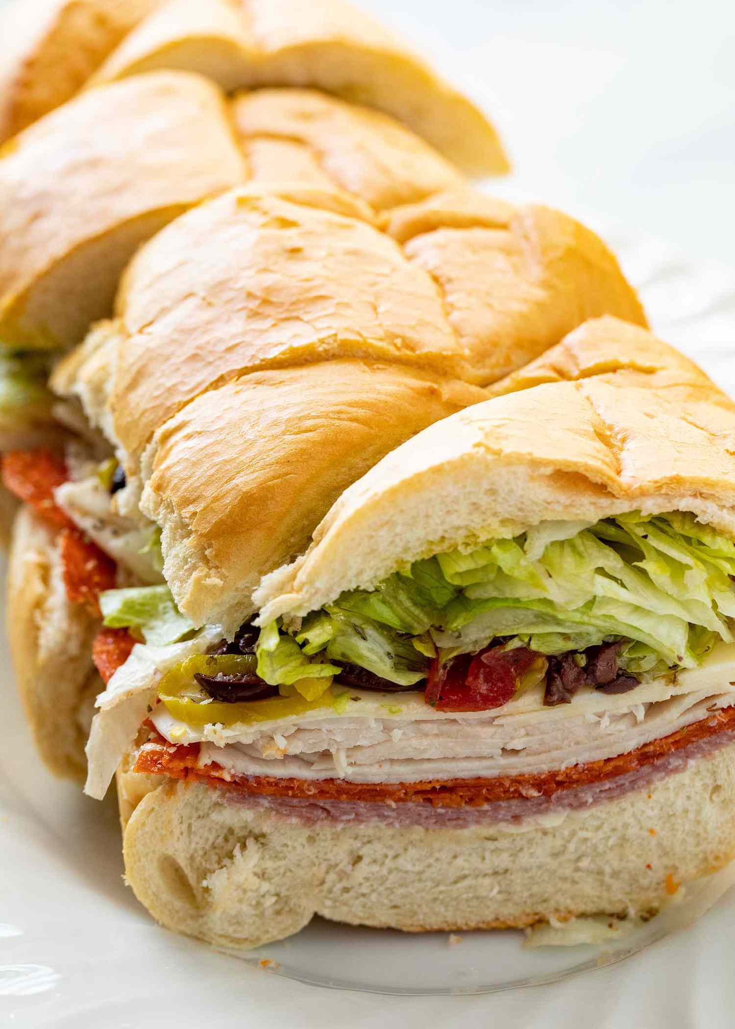 Italian sandwich for a crowd on a platter and cut into slices. Meat, cheese and toppings are layered on the sandwich.