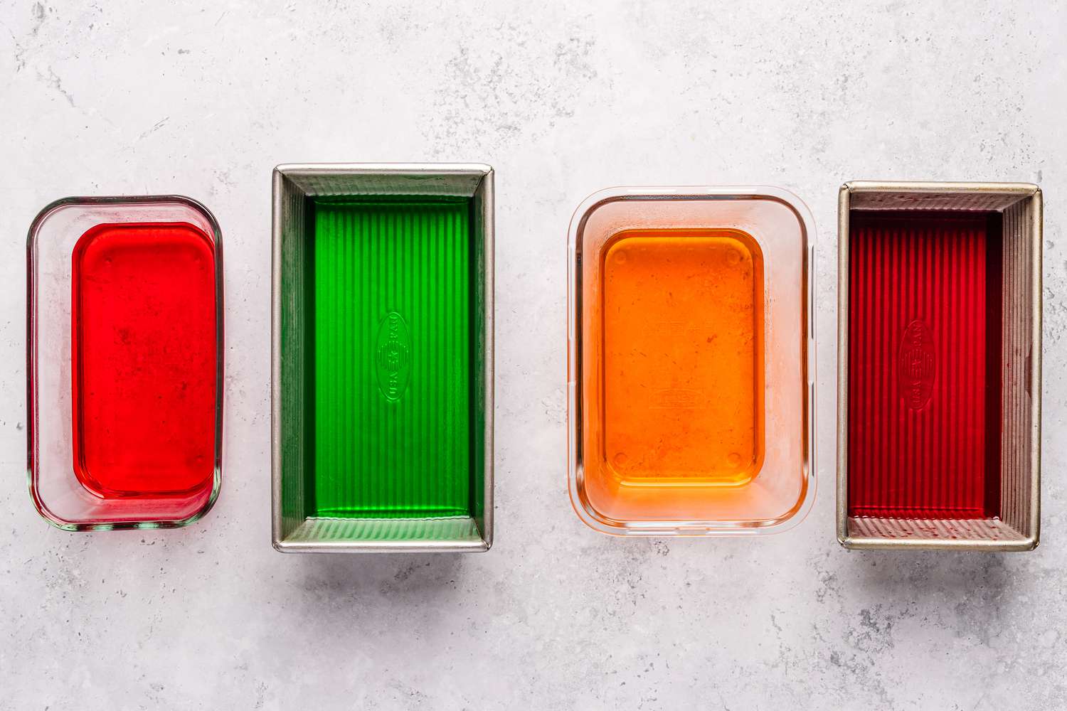 Overhead shot of four different containers with colored gelatin of red, green and orange color for stained glass jello recipe