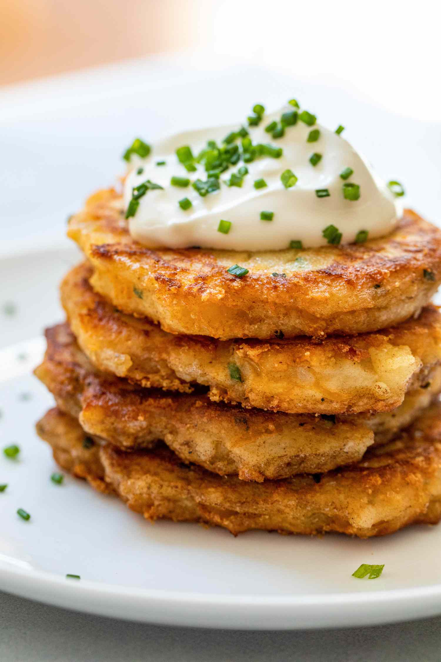 Leftover mashed potato pancakes stacked on a plate and topped with sour cream and chives.